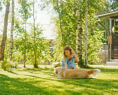 Girl playing in tree-filled yard with a dog